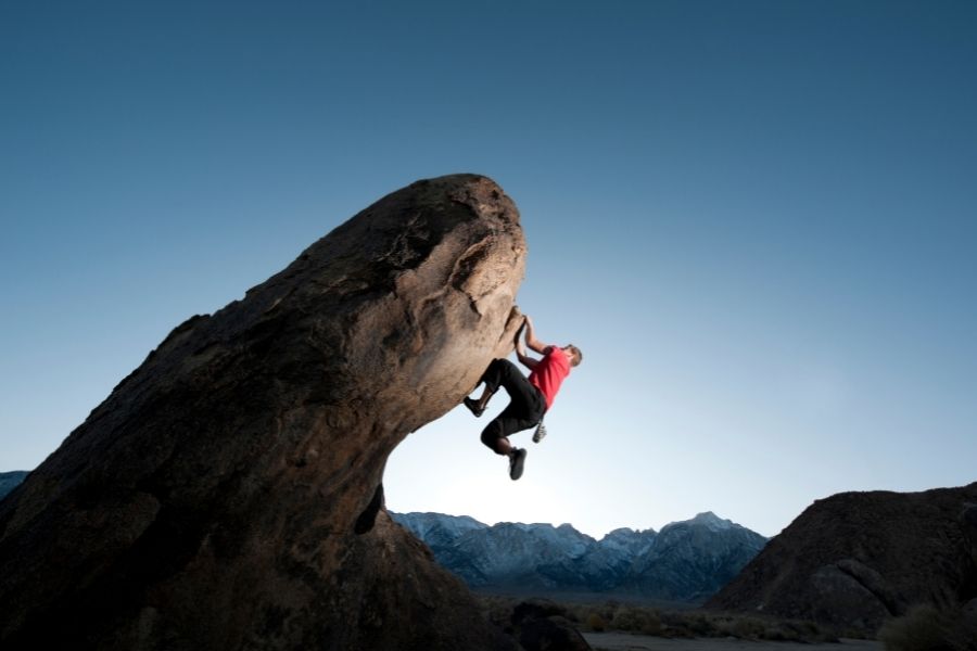 A man rock climbing and dangling from a rock iat sunset